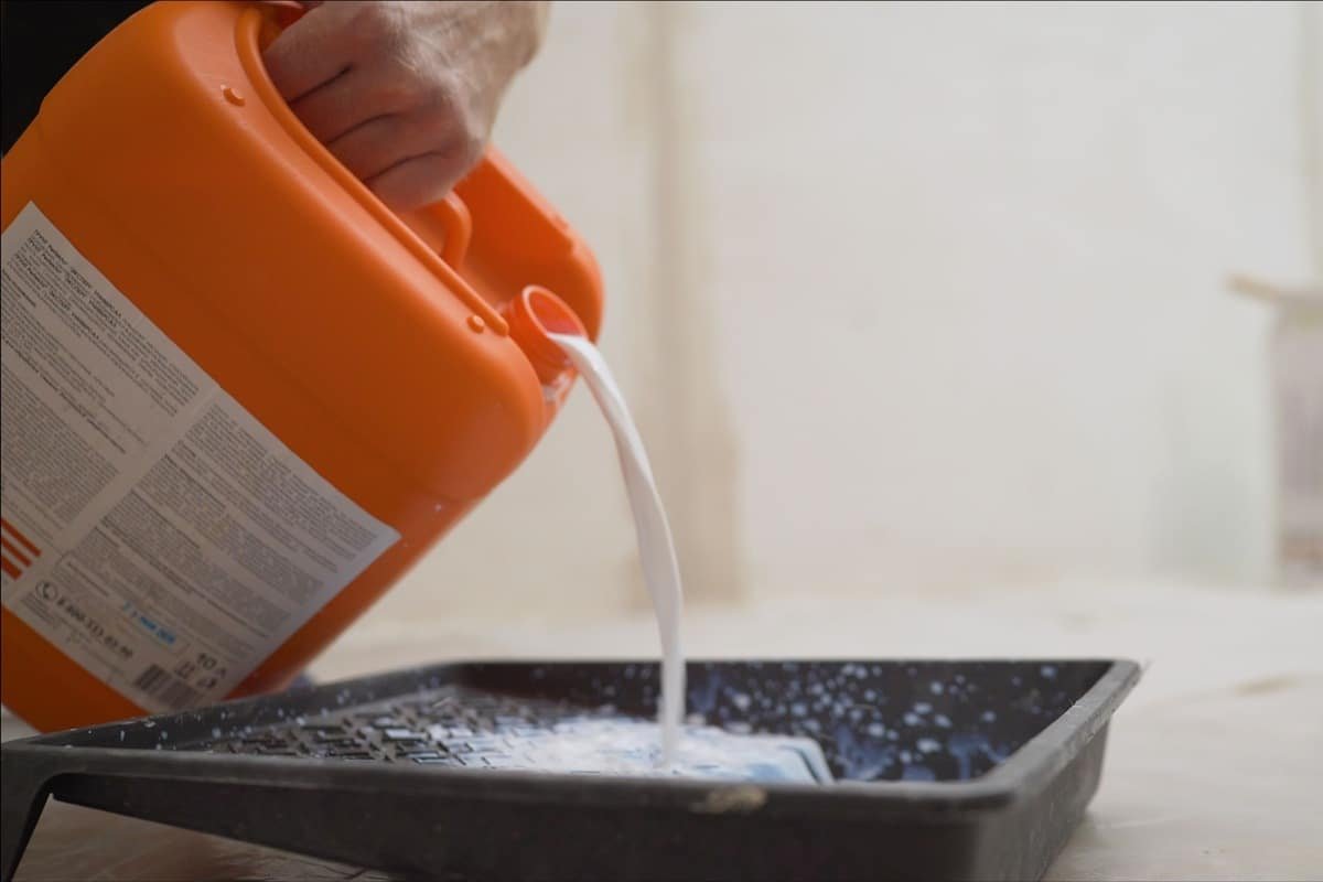 A worker pours a primer from an orange canister.. Worker pouring a primer in a paint tray